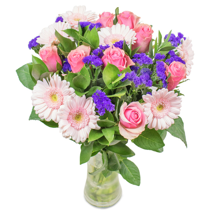 A vibrant, skillfully arranged bouquet awaits in a clear glass vase upon a pristine white background-a signature creation by Flowers Reading. The heart of the composition features an abundance of seven to nine soft and medium pink roses, each bearing tightly furled petals or beginning to reveal their elegant spirals, recalling moments of celebration throughout Reading's welcoming neighbourhoods. Five to seven pale pink gerbera daisies, their round heads and layers of petals surrounding subtly lighter centres, offer a cheerful embrace. Scattered throughout, clusters of bold, deep purple statice resemble gems nestled among petals, lending both textural interest and a pop of vivid colour reminiscent of Reading's riverside blooms. Thick green foliage forms a lush, abundant base, their freshness mirroring the parkland that edges the city. The clear vase, with its visible stems and water, enhances the design's sense of vitality and freshness. Ideal for occasions-from birthdays to anniversaries, or as a stylish enhancement for a Reading office or home-this arrangement conveys joy, warmth, and a touch of elegance unique to the local area.