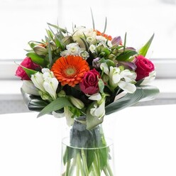 With an eye toward harmony and vibrancy, this bouquet is a showcase of Reading's floral refinement. The composition begins with wide, orange-hued gerbera daisies-each petal radiating strength and optimism-set against the gentle tranquillity of peach-coloured varieties. Interplaying with these are deep magenta roses, their lush spirals bringing a soulful complexity, joined by white alstroemeria and dainty spray roses that lend the entire bouquet a luminous freshness. Gentle touches of pastel pink and the filigree of ethereal white filler flowers thread throughout, echoing the layered abundance of Reading's public gardens. Framing the bouquet are glossy, broad aspidistra leaves, their rich green curving upward to provide both unity and a gentle, enveloping embrace, while smaller, pointed leaves interject spring-like energy and structure. The bouquet stands proudly in a tall, clear vase, showcasing the vivid green stems as if freshly gathered from Reading's own flower markets. Subtle, diffuse lighting creates a tranquil atmosphere, highlighting every nuance of colour and form. This bouquet feels perfectly suited for marking a new beginning, honouring a loved one in Caversham, or offering beauty to a home along Oxford Road. Every bloom reveals the skill and attention to detail that defines Flowers Reading's bespoke creations.